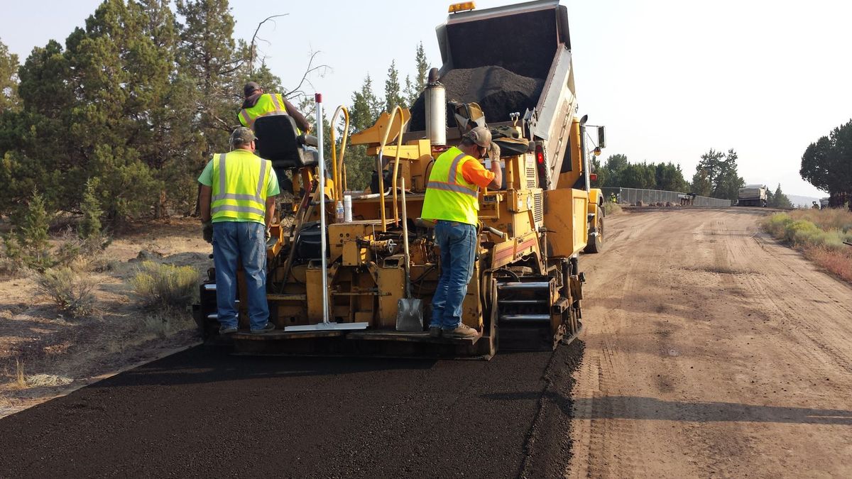 Paving crew laying fresh asphalt with a paver and dump truck
