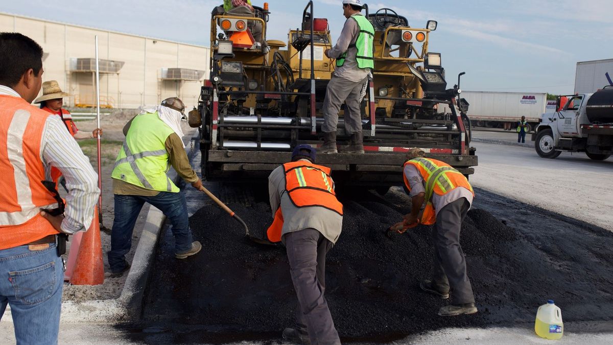 Crew raking hot asphalt into a repair area behind a paver