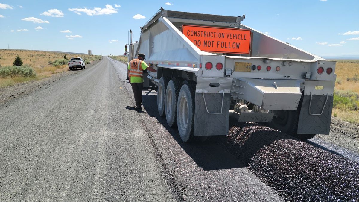 Truck spreading stone chips onto a freshly sprayed rural road